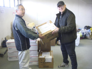 In this photo provided by Joseph Roginski, taken May 13, 2011, Joseph Roginski, right, holds a package in a storeroom of the Misawa City Hall in Japan, where donations of clothing and supplies were being kept for earthquake relief efforts. He says that while the cost of living is higher in Japan, access to health care is not. “Things are very expensive here. It is impossible to live off Social Security alone,” said Roginski, who was stationed in Japan in 1968. “But health insurance is a major factor in staying here.” The former military language and intelligence specialist said he pays $350 annually to be part of Japan’s national health insurance. His policy covers 70 percent of his costs. The rest is covered by a secondary insurance program for retired military personnel. (Joseph Roginski via AP)