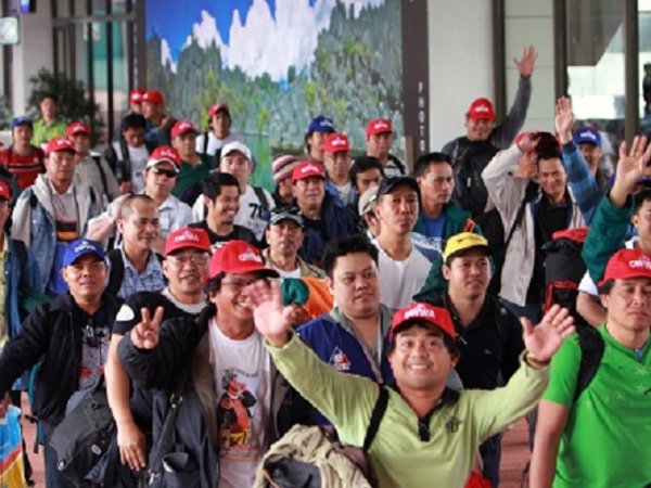 OFW with raised arms, posing for a photo with other workers
