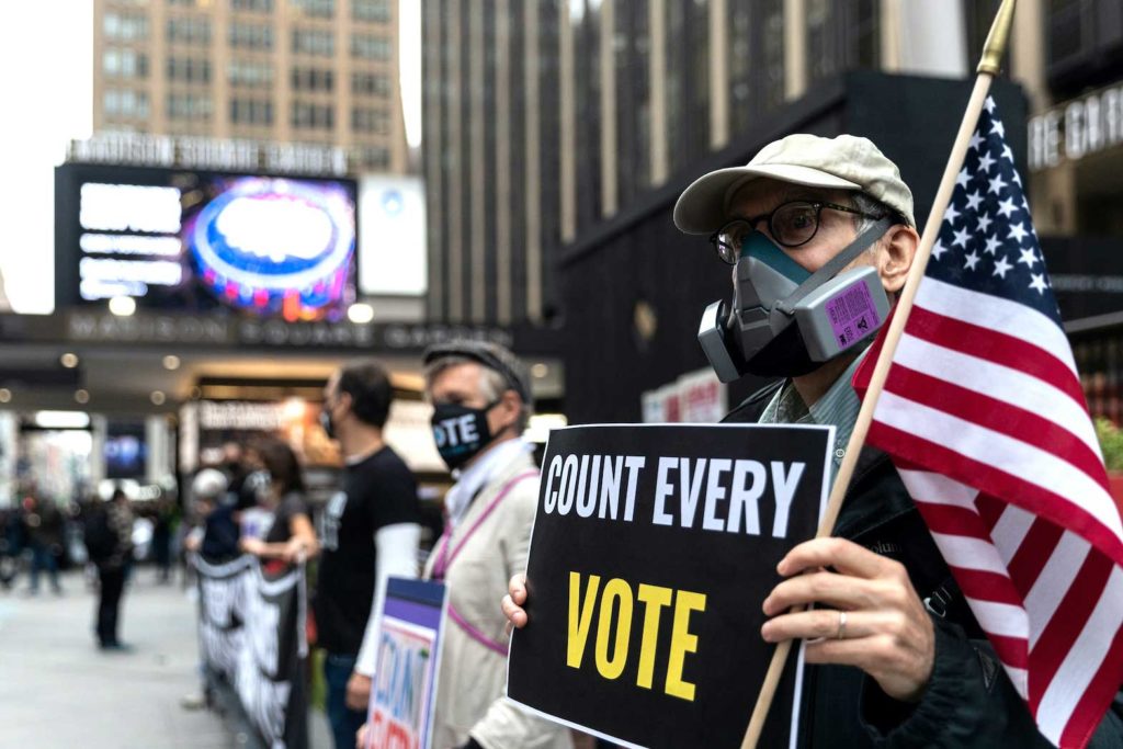 A man wearing a protective mask due to COVID-19 pandemic holds a sign outside Madison Square Garden, which is used as a polling station, on the first day of early voting in Manhattan, New York, U.S. October 24, 2020. REUTERS/Jeenah Moon