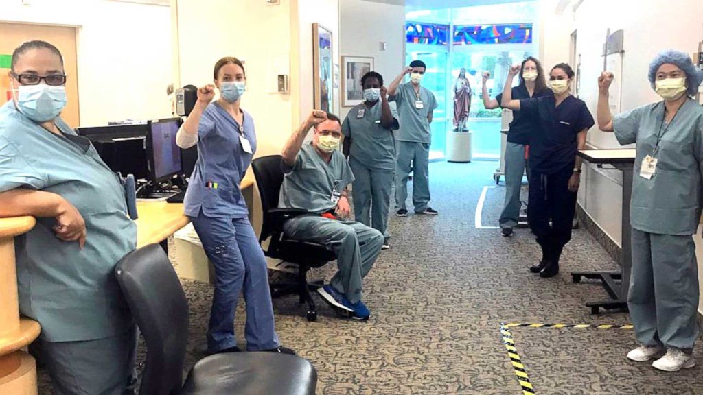 In this image provided by Lizabeth Baker Wade, nurses at Providence Saint John's Health Center in Santa Monica, Calif., on April 10, 2020, raise their fists in solidarity after telling managers they can't care for Covid-19 patients without N95 respirator masks to protect themselves. The hospital has suspended ten nurses from the ward, but has started providing nurses caring for Covid-19 patients with N95 masks. (Lizabeth Baker Wade via AP)