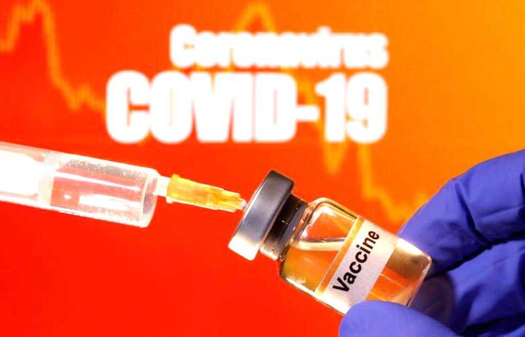 A small bottle labeled with a "Vaccine" sticker is held near a medical syringe in front of displayed "Coronavirus COVID-19" words in this illustration taken April 10, 2020. REUTERS/Dado Ruvic/Illustration