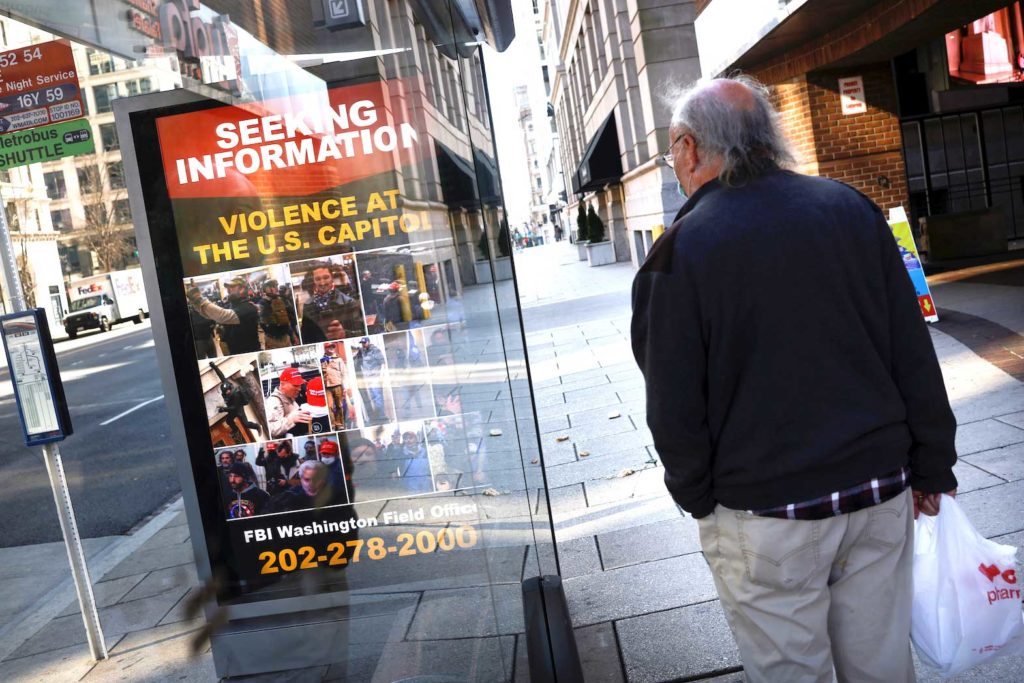   A local resident looks at a billboard with pictures of supporters of U.S. President Donald Trump wanted by the FBI who participated in storming the U.S. Capitol, forcing Congress to postpone a session certifying the results of the 2020 U.S. presidential election, in Washington, U.S., January 13, 2021. REUTERS/Carlos Barria
