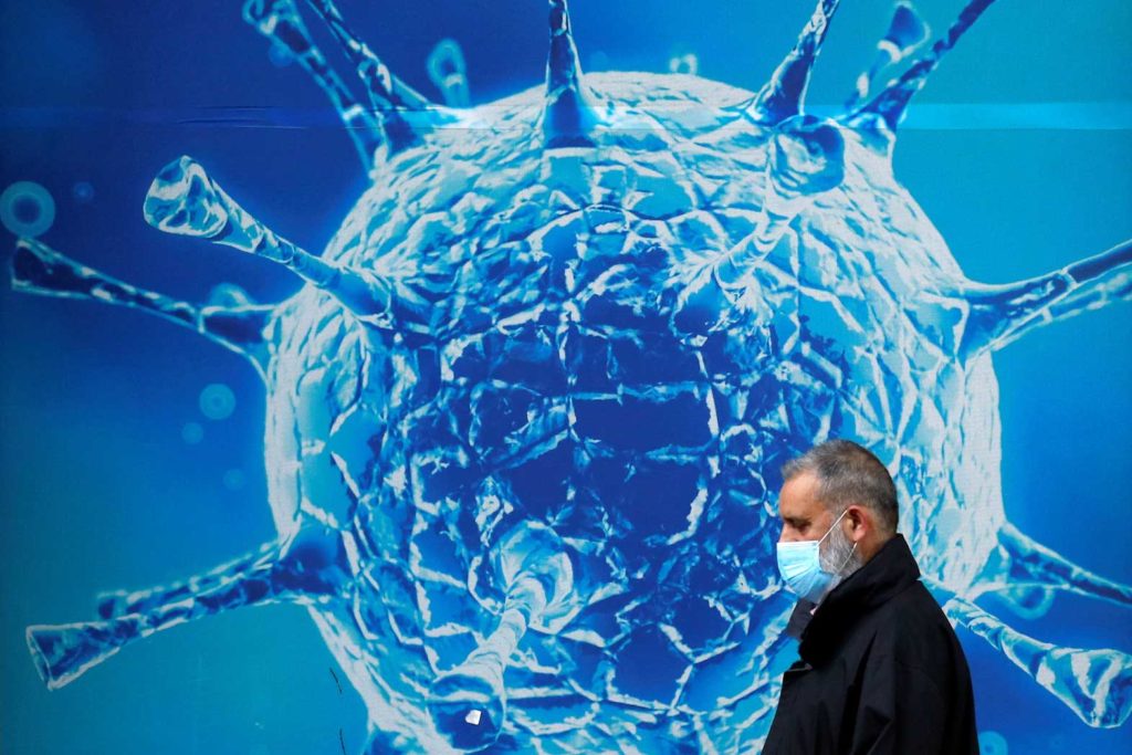 A man wearing a protective face mask walks past an illustration of a virus outside a regional science centre, as the city and surrounding areas face local restrictions in an effort to avoid a local lockdown being forced upon the region, amid the coronavirus disease (COVID-19) outbreak, in Oldham, Britain August 3, 2020. REUTERS/Phil Noble