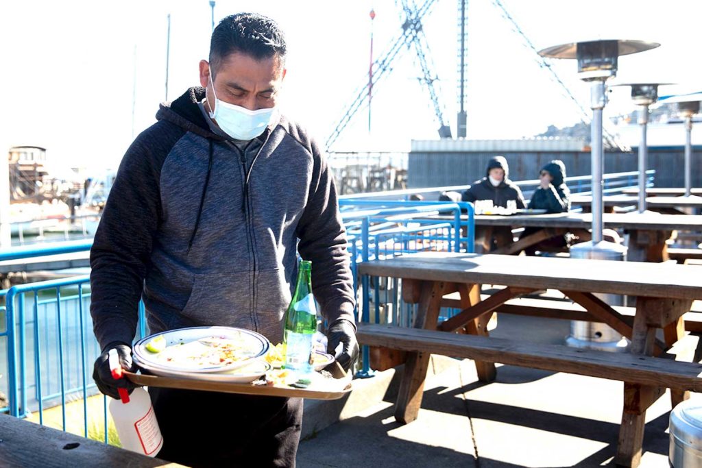 Victor Garcia works to disinfect tables and clear finished plates at Fish restaurant in Sausalito, California, on Jan. 25. Fish was one of the first restaurants to re-open for outdoor dining after Governor Gavin Newsom lifted shelter-in-place orders. KHN