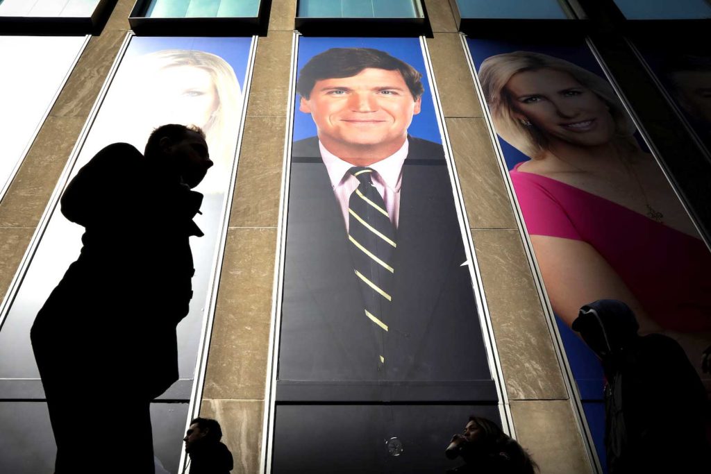 People pass by a promo of Fox News host Tucker Carlson on the News Corporation building in New York, U.S., March 13, 2019. REUTERS/Brendan McDermid