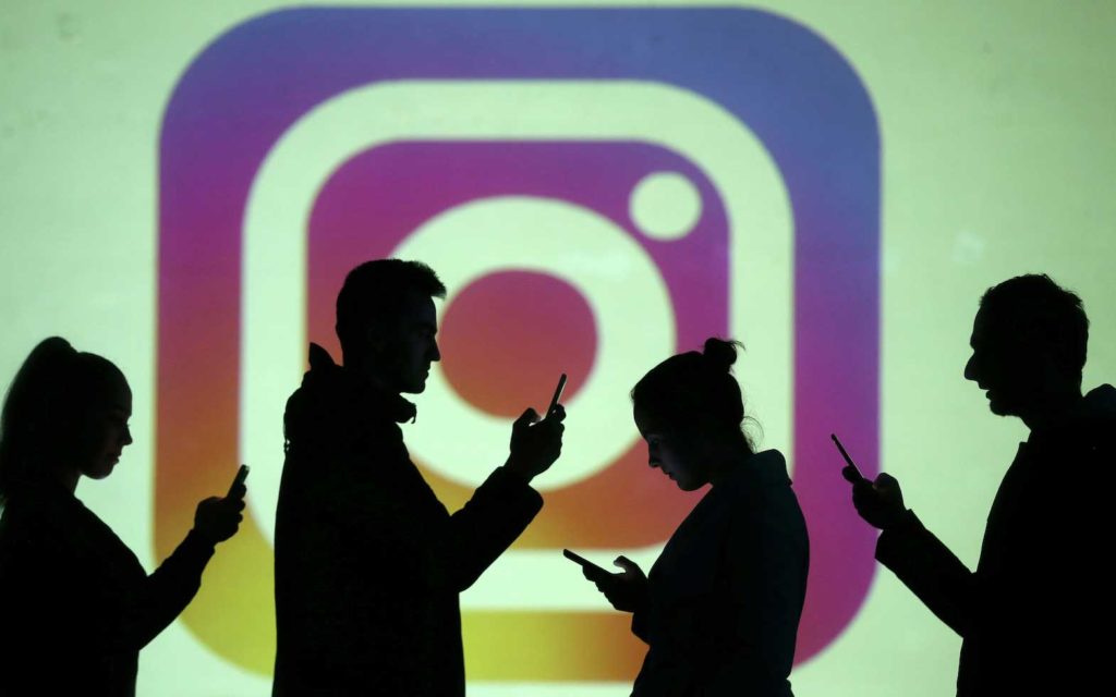 Silhouettes of mobile users are seen next to a screen projection of Instagram logo in this picture illustration taken March 28, 2018. REUTERS/Dado Ruvic/Illustration/File Photo