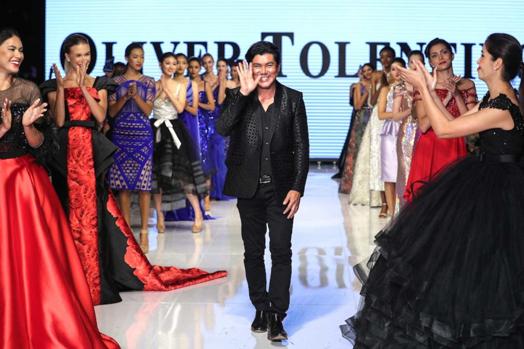 Oliver grinning with hand up in final walk at Oliver Tolentino LAFW 2021 Runway Event at LA Petersen Automotive Museum. CONTRIBUTED