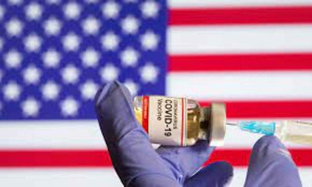 A woman holds a small bottle labeled with a "Coronavirus COVID-19 Vaccine" sticker and a medical syringe in front of displayed USA flag in this illustration taken, October 30, 2020. REUTERS/Dado Ruvic