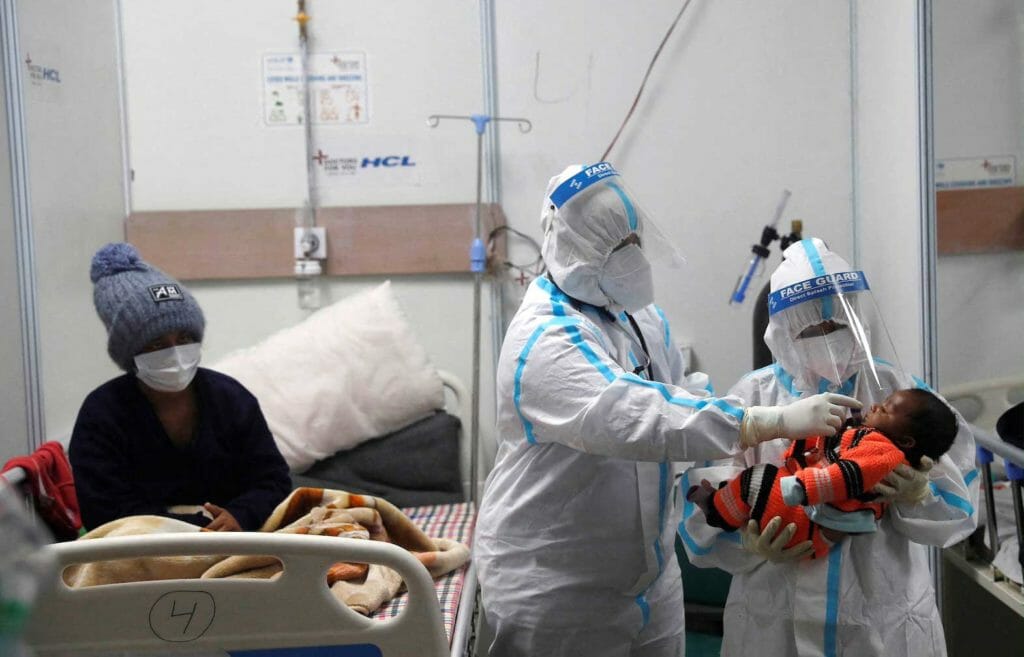 Medical workers wearing personal protective equipment (PPE) check temperature of an infant, whose mother is suffering from coronavirus disease (COVID-19), inside a care centre at an indoor sports complex, amidst the spread of the disease, in New Delhi, India, January 5, 2022. REUTERS/Adnan Abidi