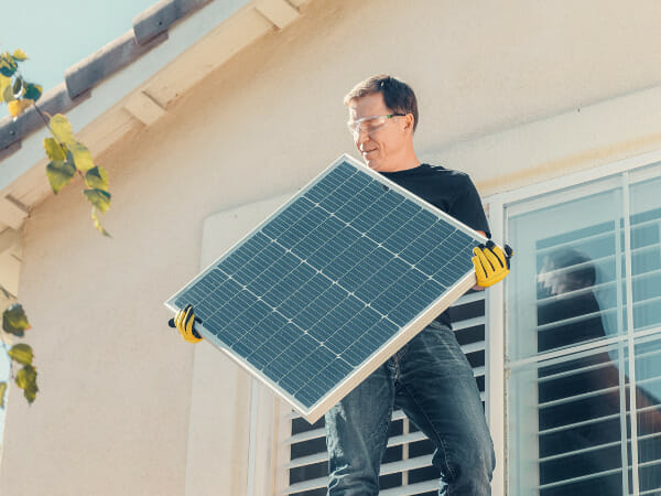 This is a person carrying a solar panel while standing on a roof.