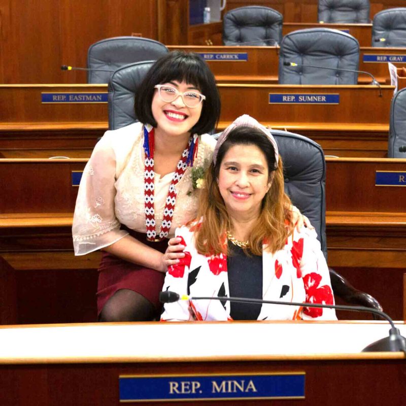 Rep. Genevieve Mina stands next to her mother, Evelyn Mina, in her daughter’s seat on the Alaska Legislature’s House floor. CONTRIBUTED PHOTO