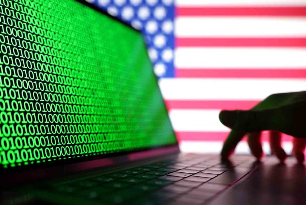A hand is seen on a laptop with binary codes displayed in front of the USA flag in this illustration taken, August 19, 2022. REUTERS/Dado Ruvic/Illustration