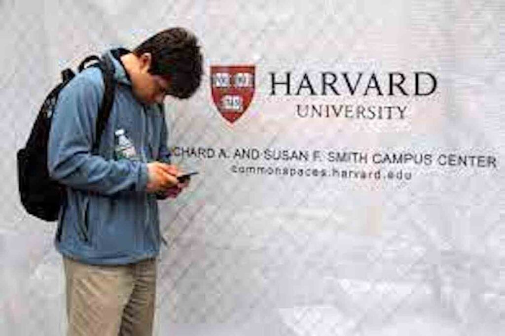A man looks at his mobile phone beside a sign for Harvard University in Cambridge, Massachusetts, U.S., June 18, 2018. REUTERS/Brian Snyder