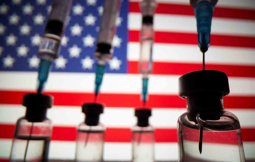 Vials and syringes are seen in front of displayed U.S. flag in this illustration photo taken March 16, 2021. REUTERS/Dado Ruvic/Illustration

