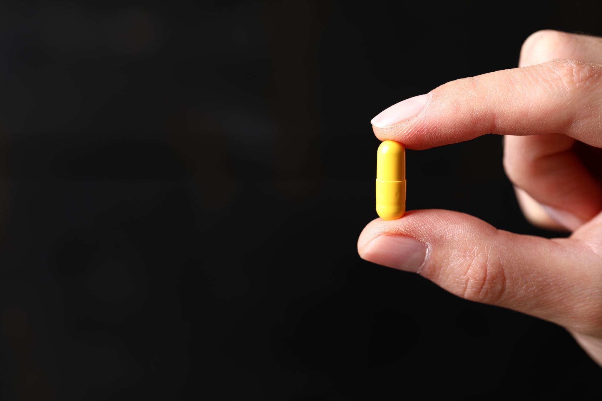Fingers holding yellow pill for ketamine therapy
