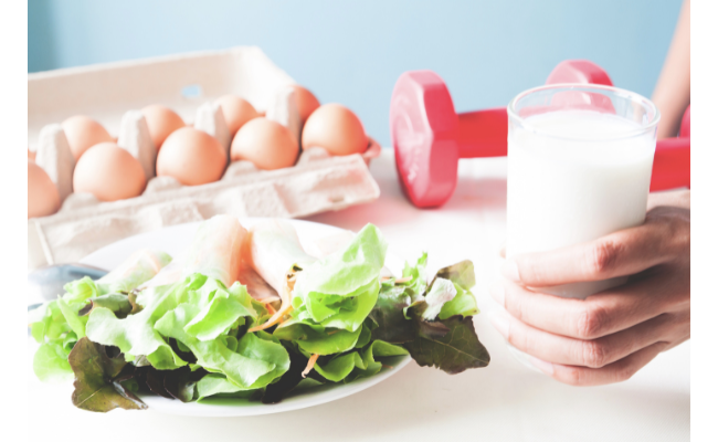 Fresh salad with carton of eggs and hand holding a glass of milk