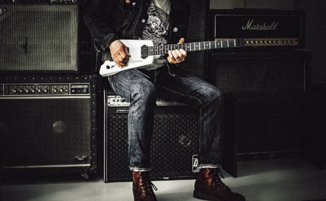 Person playing electric guitar and sitting on an amplifier wearing Doc Martens
