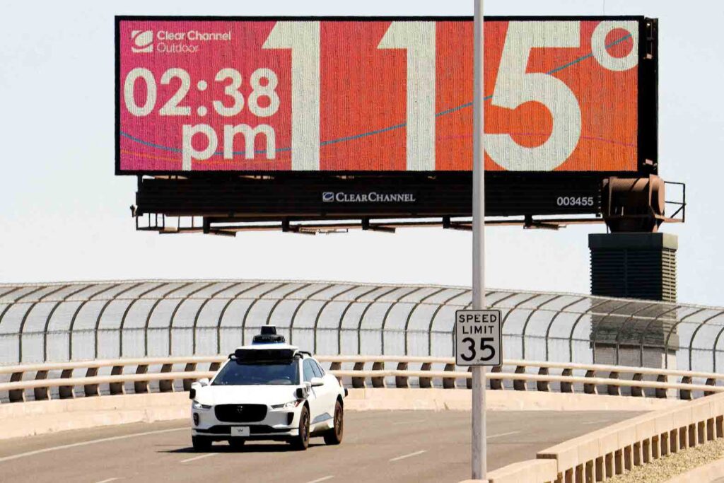 A Waymo self-driving car drives on Seventh Street as the temperature of 115 degrees is displayed on a digital billboard in downtown Phoenix, Arizona, U.S. July 17, 2023. Phoenix hit 114F (45.5C) on July 17, matching a historic record of 18 straight days over 110F with the forecast showing the record likely to extend for at least another week. Rob Schumacher/USA Today Network via REUTERS.
