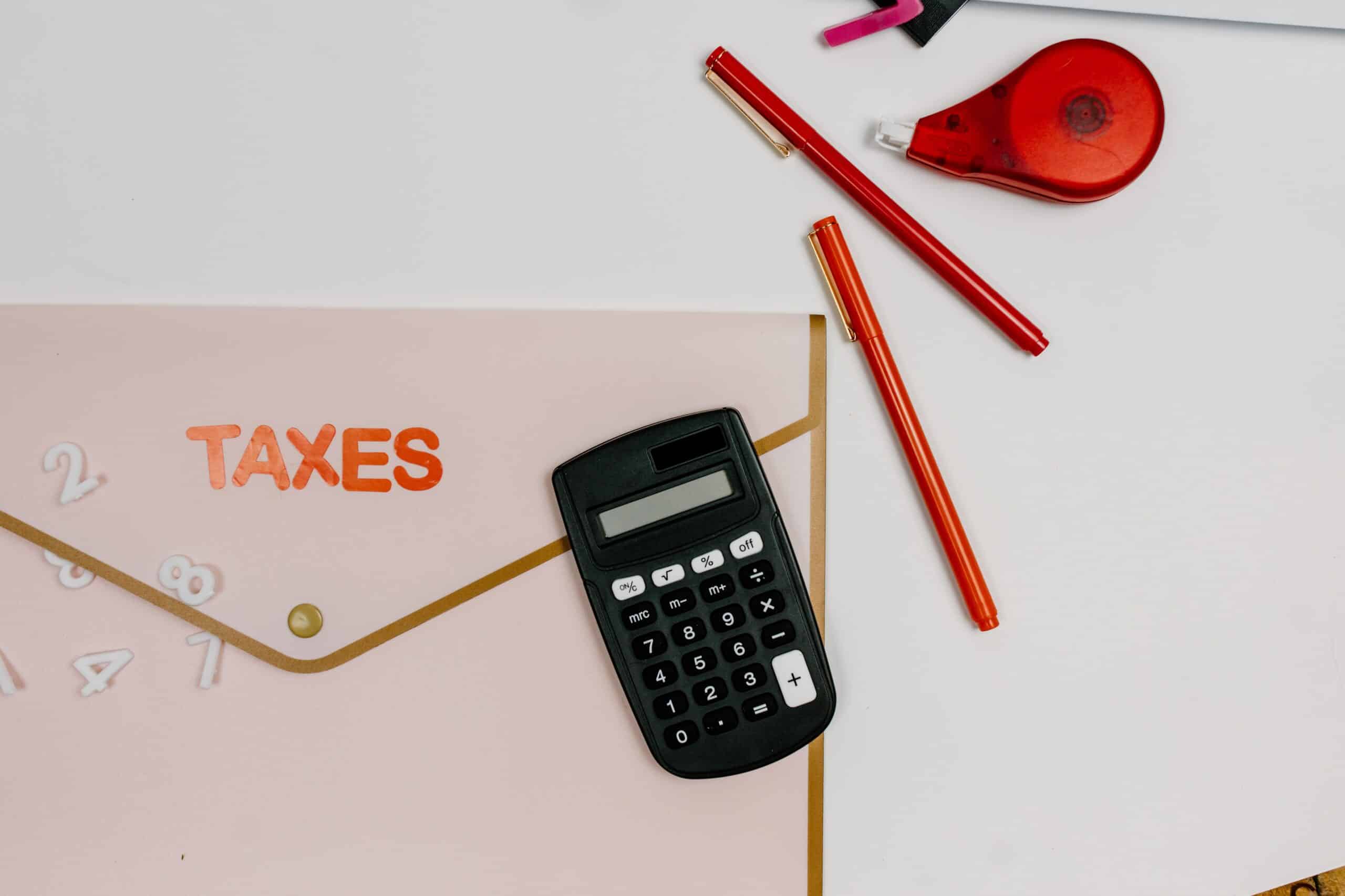 Calculator and red pens on a pink TAXES folder, representing IRS tax abatement options to reduce penalties and interest owed.