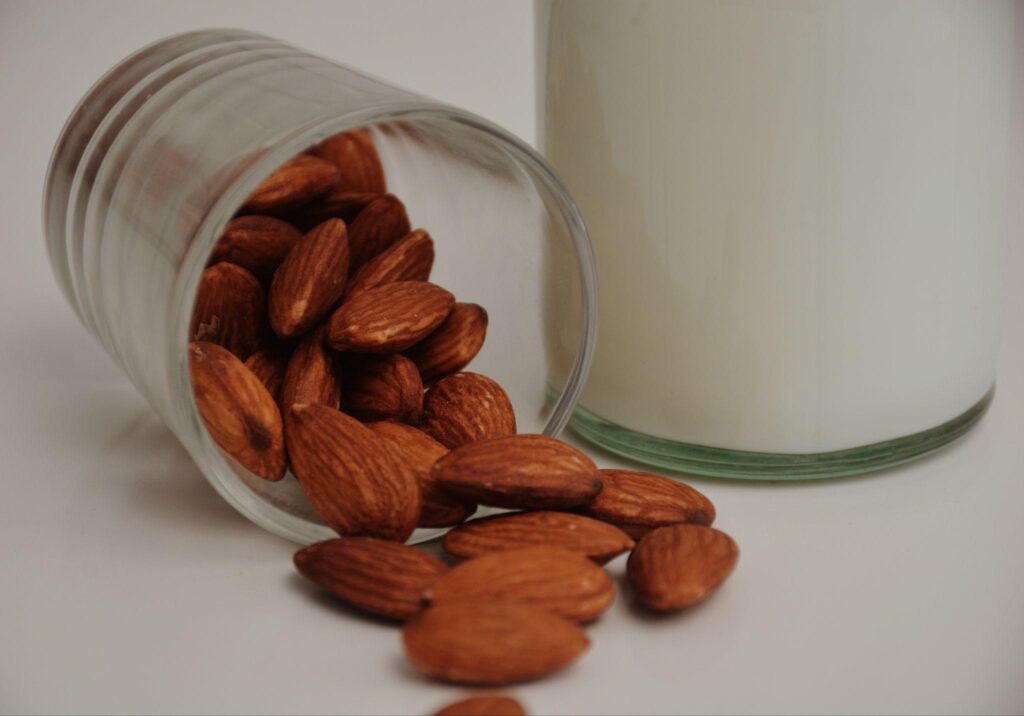 Almonds in glass knocked over next to glass of milk