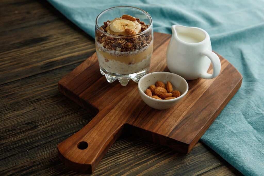 Peanut butter and banana overnight oats in glass jar with milk and nuts on a wooden board