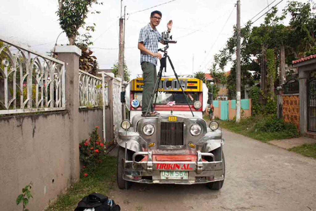 Jason Reblando standing on top of a car with a tripod in the Philippines. WEBSITE
