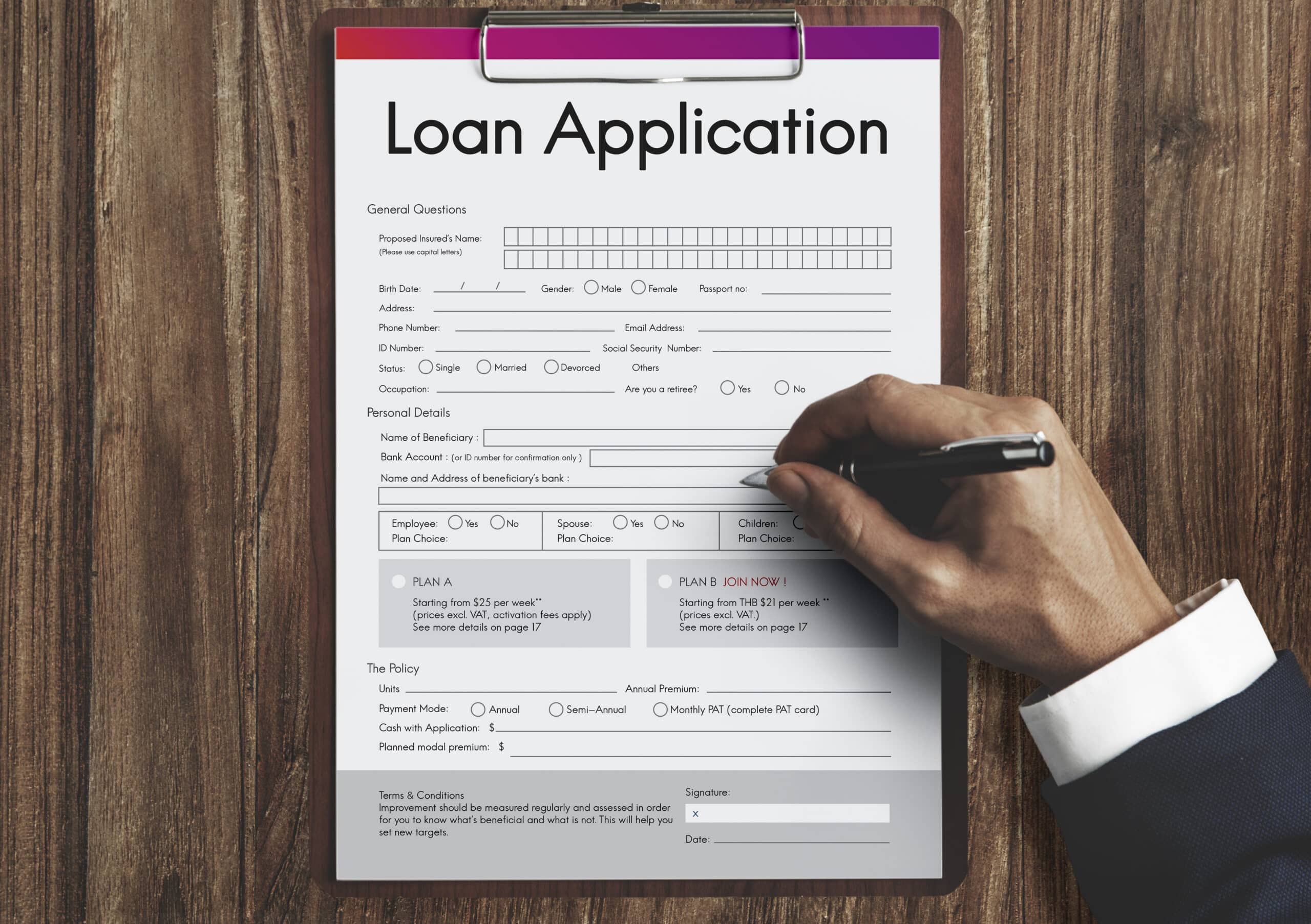 Hand filling out a loan application form on a clipboard, showing personal details, plan choices, and a signature line.
