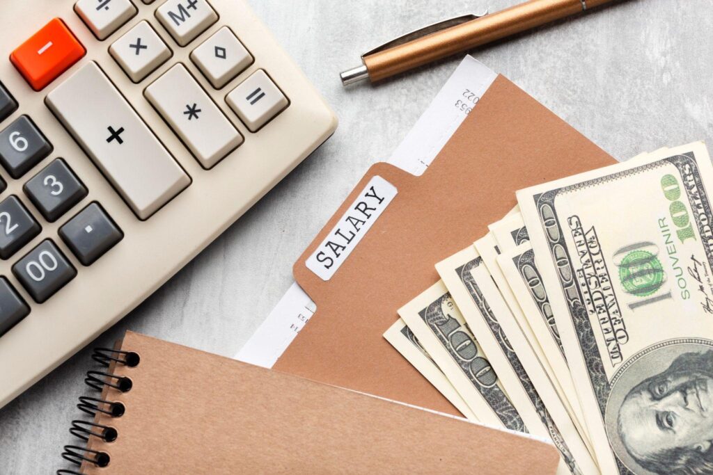 Salary folder under a notebook, cash, calculator, and pen