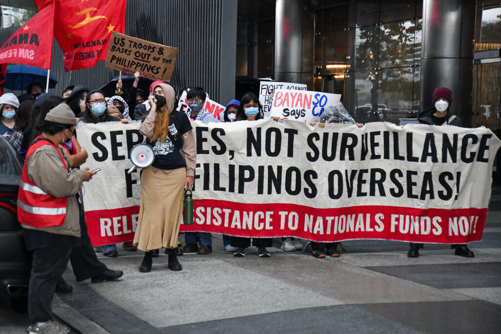 Protesters display banner saying "Services, not surveillance, for Filipinos overseas."
