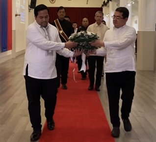 Two men on red carpet carrying wreath