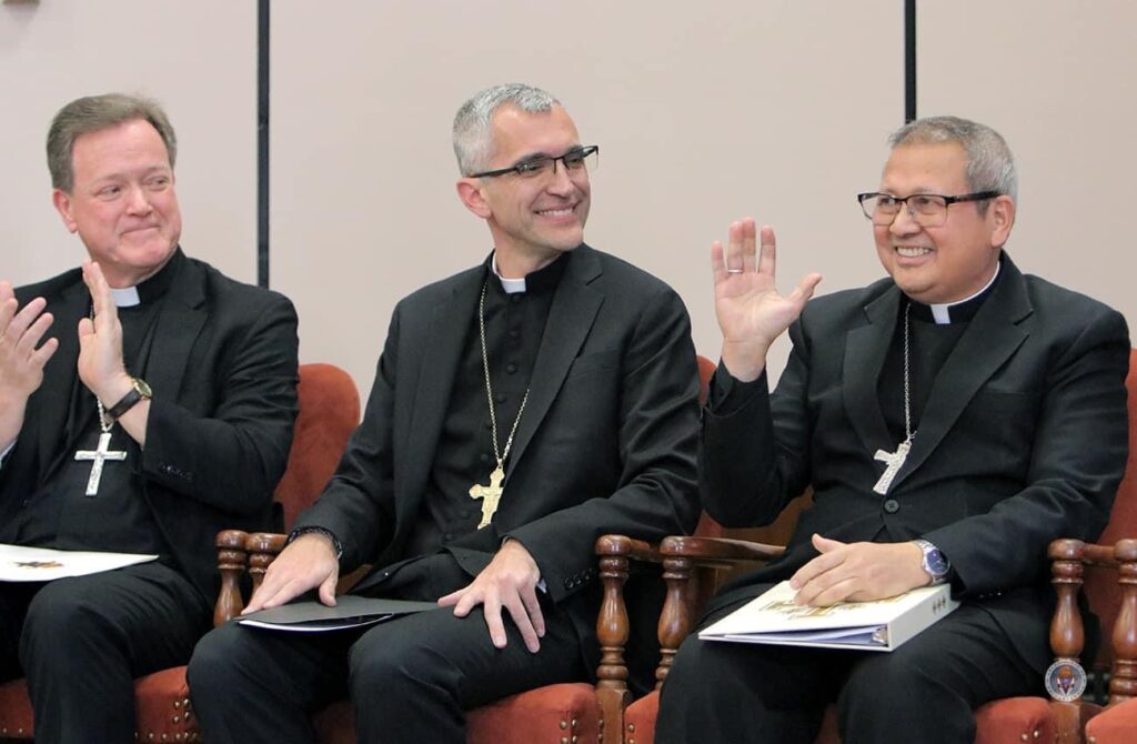 Three bishops garbed in black vestments sitting next to each other