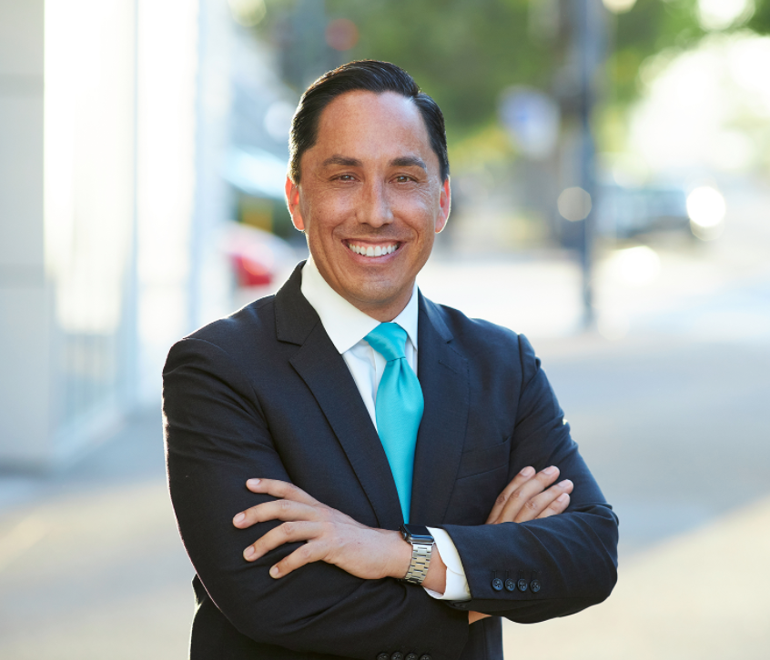 Todd Gloria wearing a dark suit with a Turquoise-colored tie