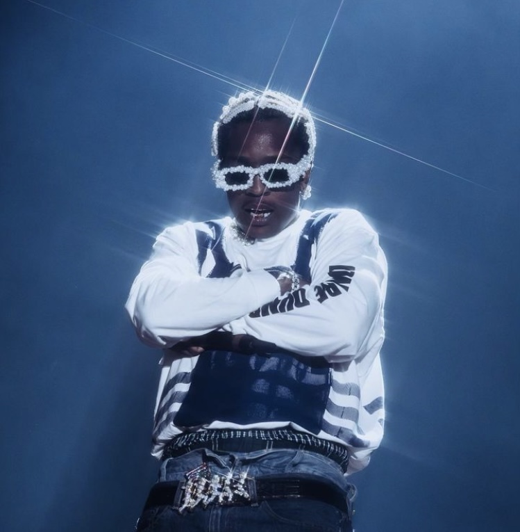 A$AP Rocky, wearing white rimmed eyeglasses, crosses arm