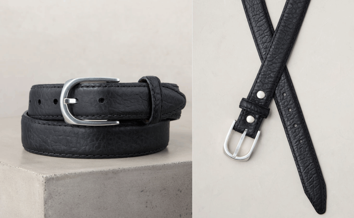 Black bison leather belt with silver buckle displayed on a textured surface.
