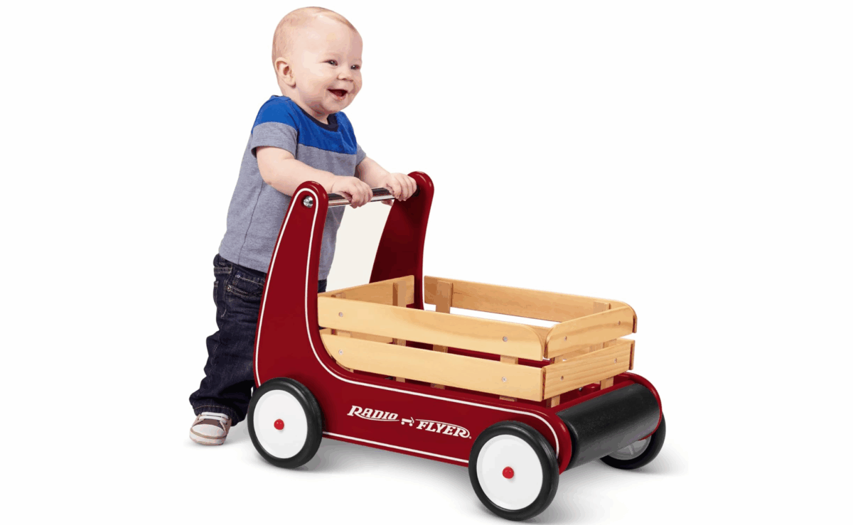 Baby pushing a red Radio Flyer wooden wagon walker with sturdy wheels.