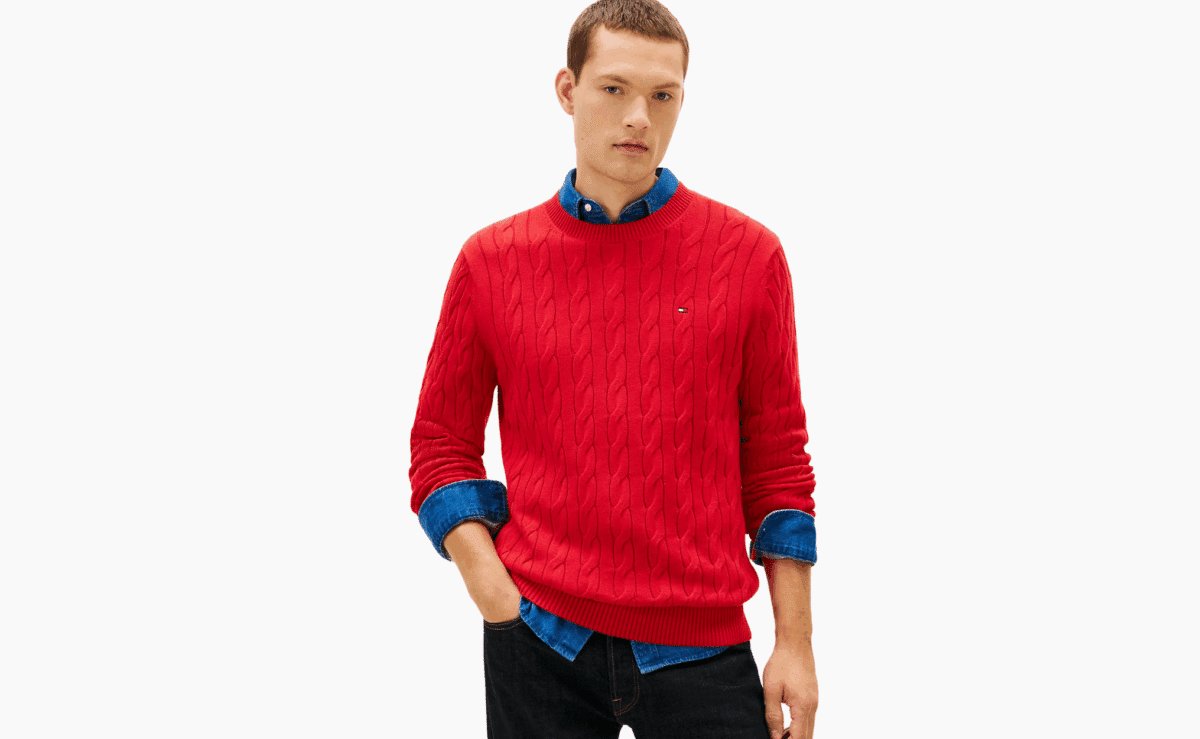 Red cable-knit crewneck sweater with textured stitching layered over a denim shirt.