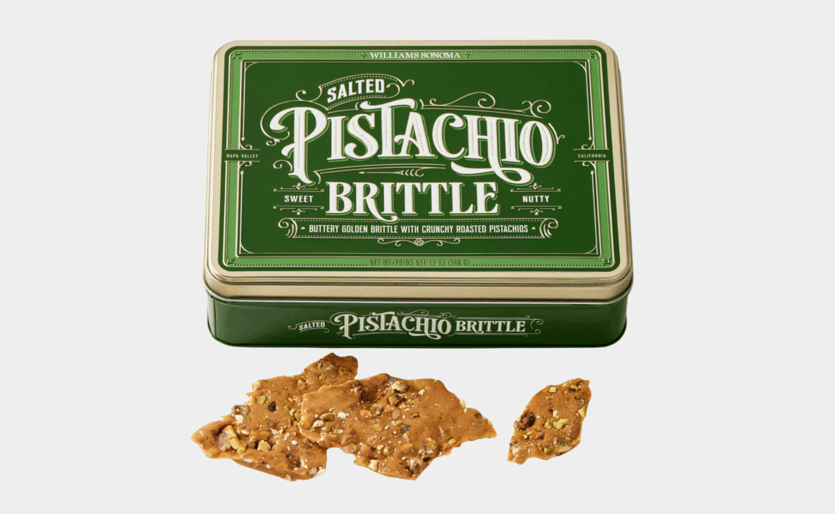 Green tin of Williams Sonoma salted pistachio brittle with brittle pieces displayed beside it.