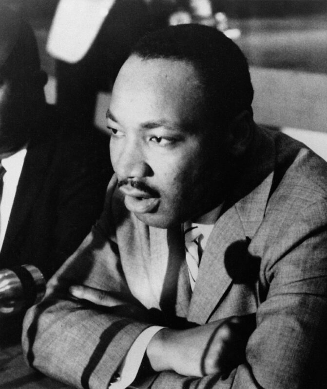 Martin Luther King Jr. with arms cross, speaking into microphone