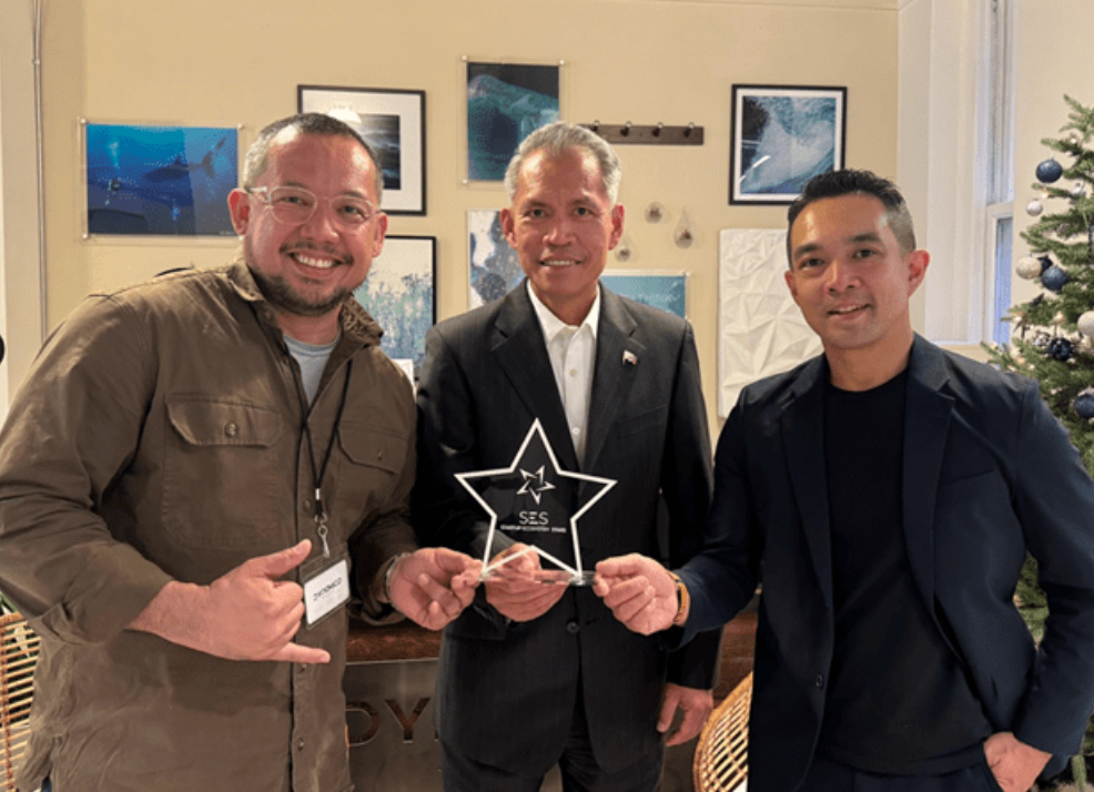 Consul General Ferrer, holding crystal plaque, between two startup founders
