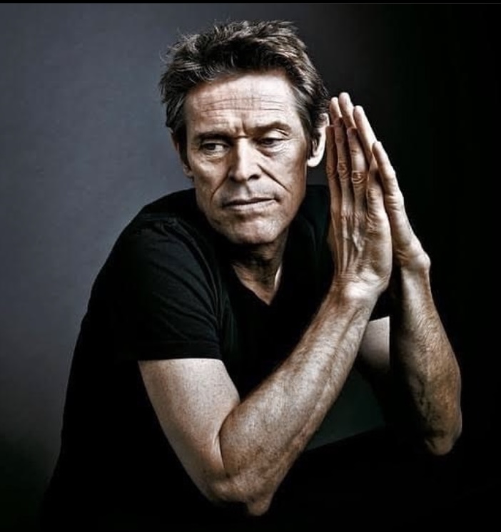Dafoe clasping his hands as if in prayer