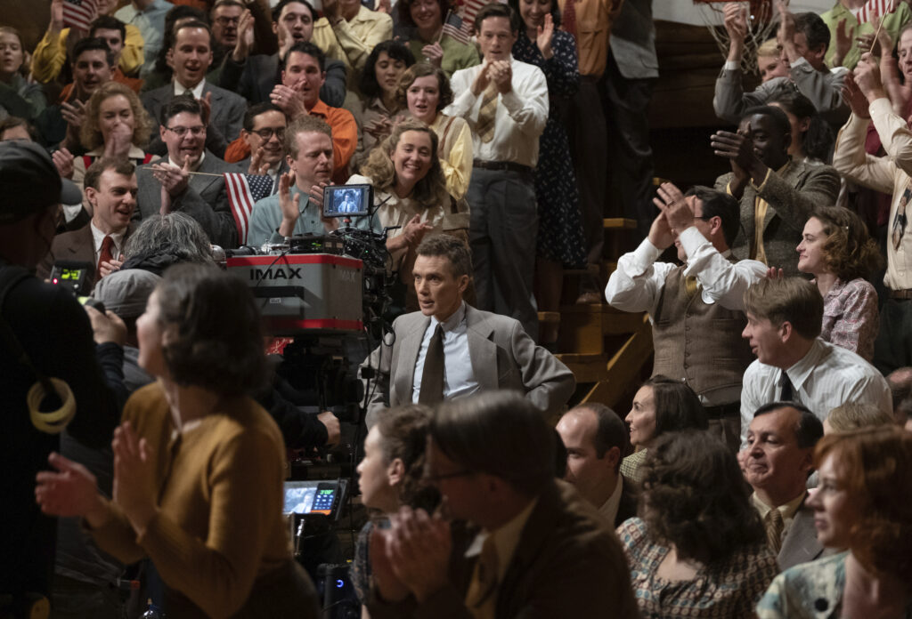 Scene from Oppenheimer, man in a suit in the middle of a crowd