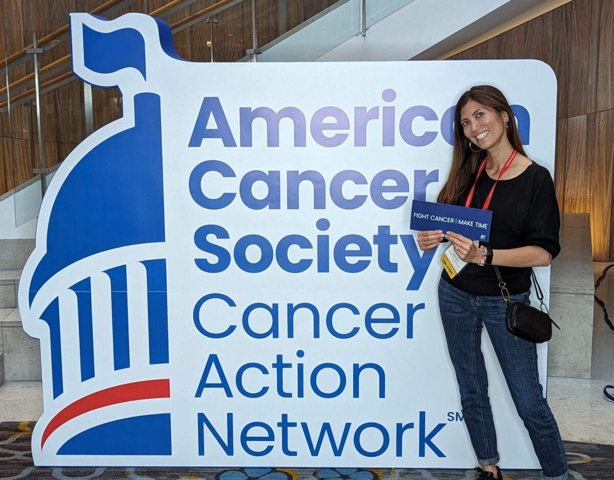 Jaimie Escoto poses next to enlarged logo of American Cancer Society Cancer Action Network