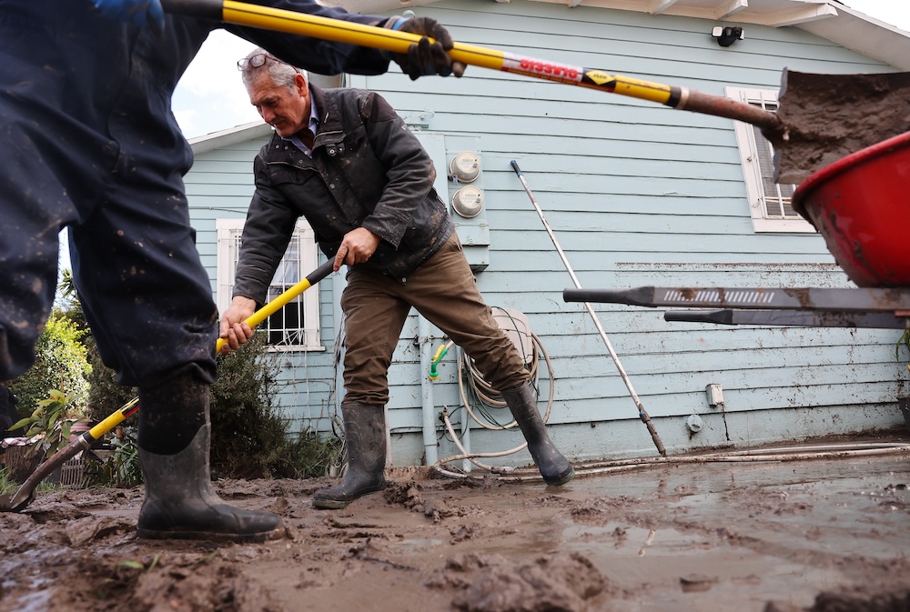 SAN DIEGO, CALIFORNIA - JANUARY 23: Family members clean mud from a home damaged by flooding, with the floodwater line visible on the house, the day after an explosive rainstorm deluged areas of San Diego County on January 23, 2024 in San Diego, California. The intense rains forced dozens of rescues while flooding roadways and homes and knocking out electricity for thousands of residents. Mario Tama/Getty Images/AFP (Photo by MARIO TAMA / GETTY IMAGES NORTH AMERICA / Getty Images via AFP)