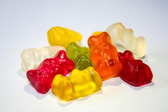 Close-up of colorful THC gummies, including red, yellow, and white pieces, displayed on a plain surface.