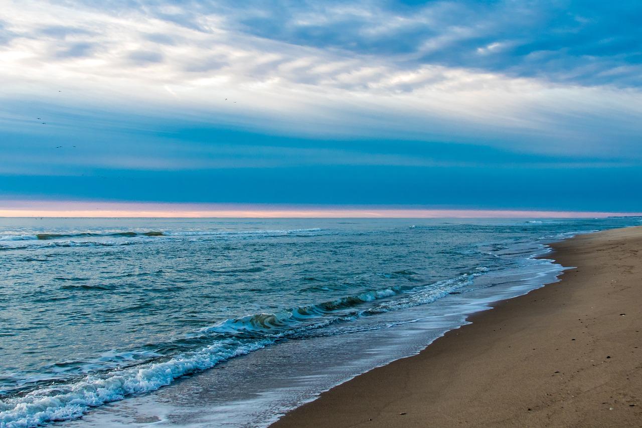 A serene view of Ngapali Beach in Myanmar, featuring gentle waves lapping against the soft sandy shoreline under a vibrant sky at dusk.