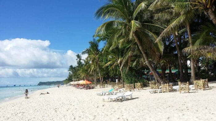 White Beach in Boracay, Philippines, with powdery white sand, palm trees, sun loungers, and a clear blue sky, perfect for relaxation and leisure.