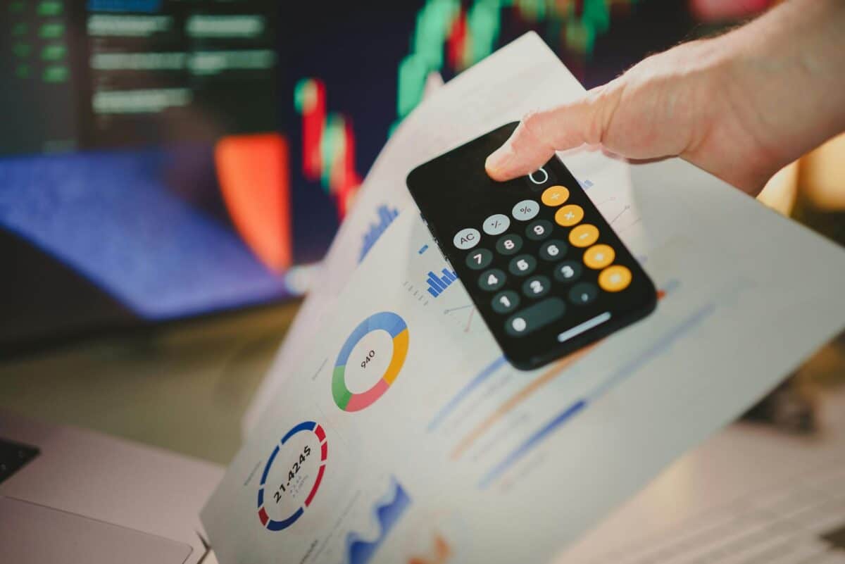 A hand holding a smartphone calculator over financial charts and graphs, symbolizing loan application and financial planning with OneMain Financial