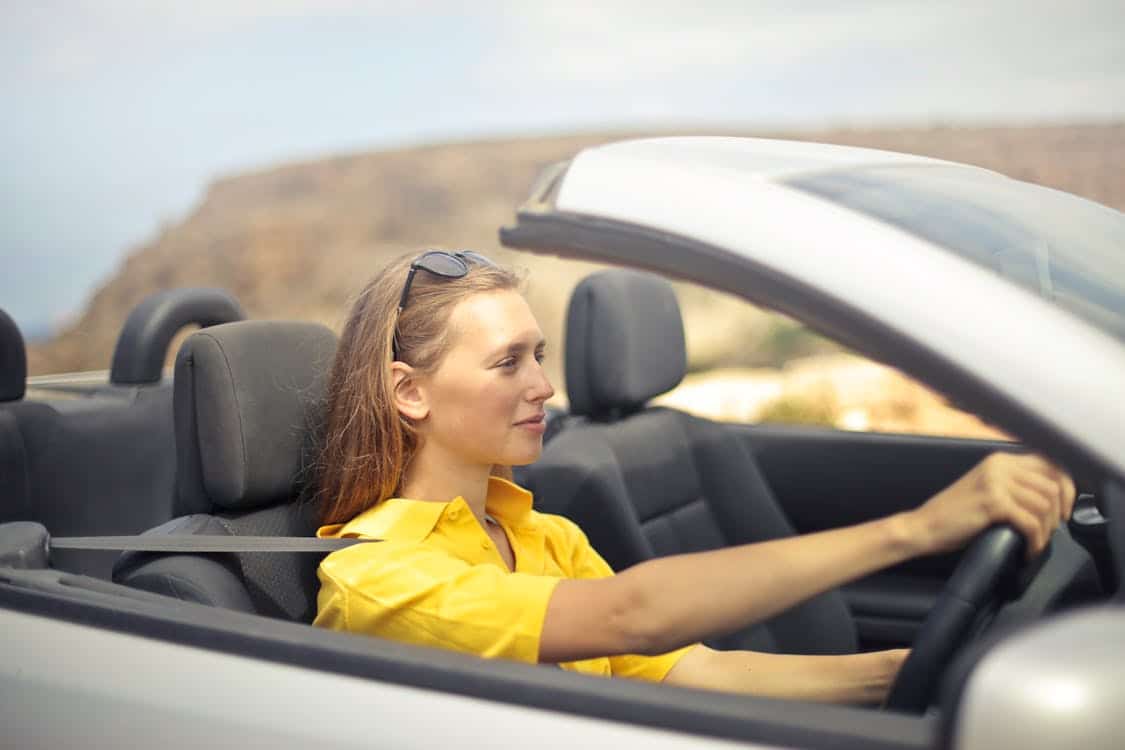 Smiling woman driving a convertible car, featured in an article section summarizing positive and negative customer reviews of Capital One Auto Financing, focusing on communication, accessibility, and customer experience.
