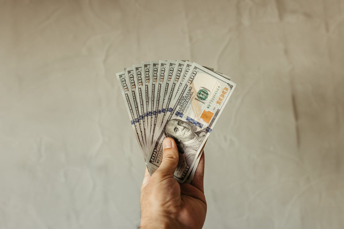 Hand holding a fan of hundred-dollar bills, representing loan amounts, interest costs, and financial borrowing through lenders like Republic Finance