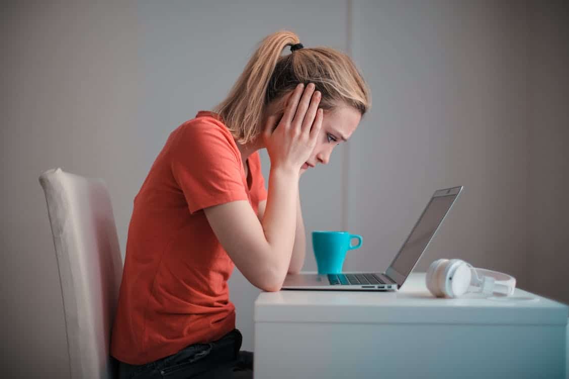 Worried woman sitting at a desk with laptop and coffee, symbolizing financial stress and the decision to apply for a personal loan with Regional Finance.